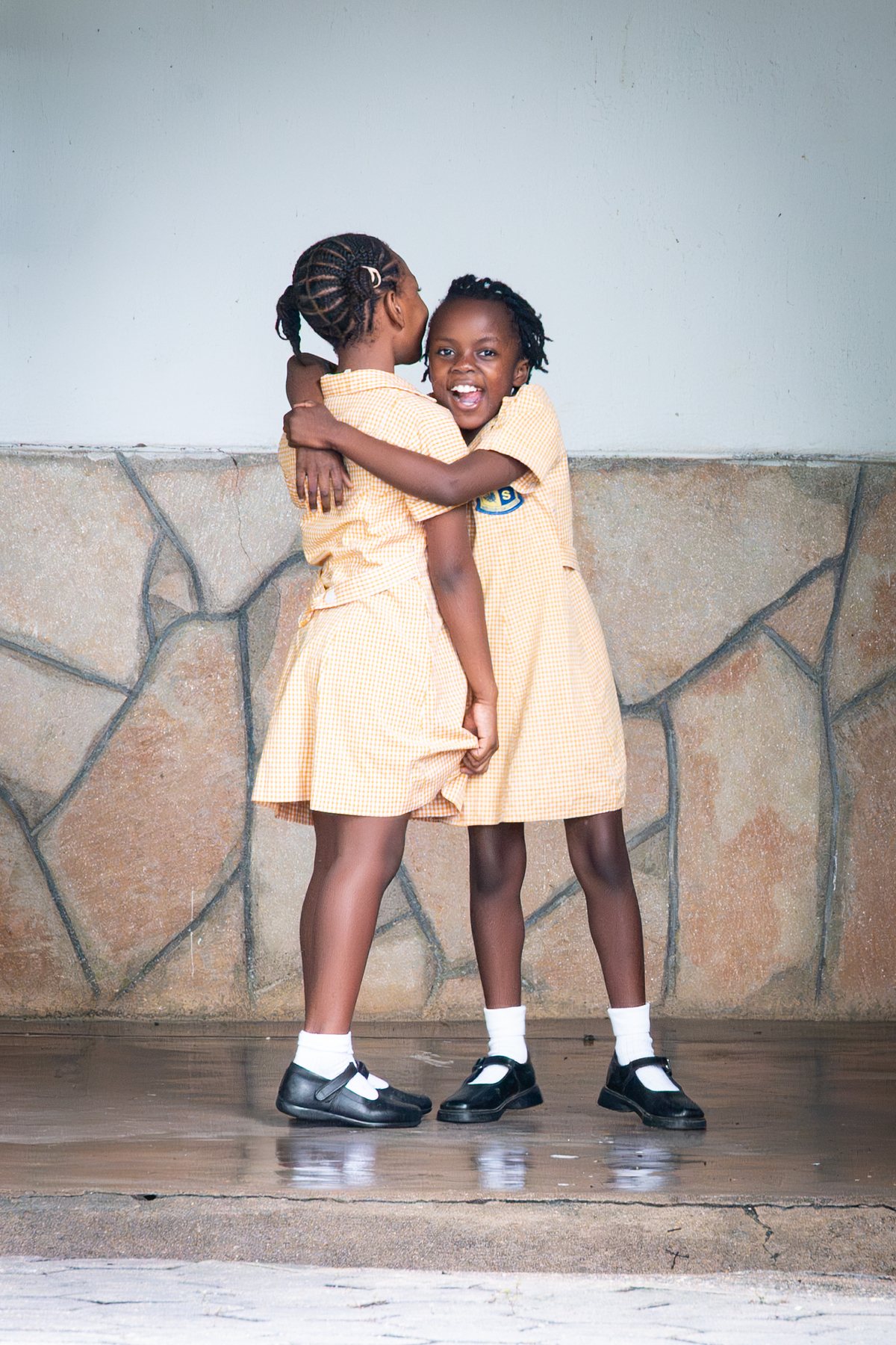 Two Musikili pupils in uniform hugging outside the classroom in the first week of term